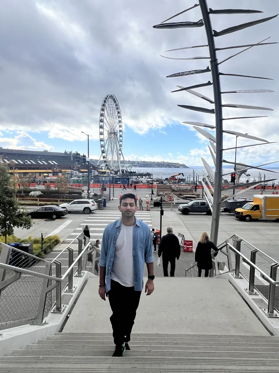 Akshit walking up the steps near the Seattle waterfront, ferris wheel behind